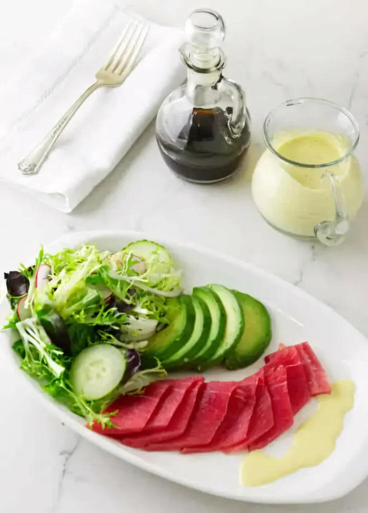 Tuna sashimi on a plate next to a green salad and a wasabi emulsion.