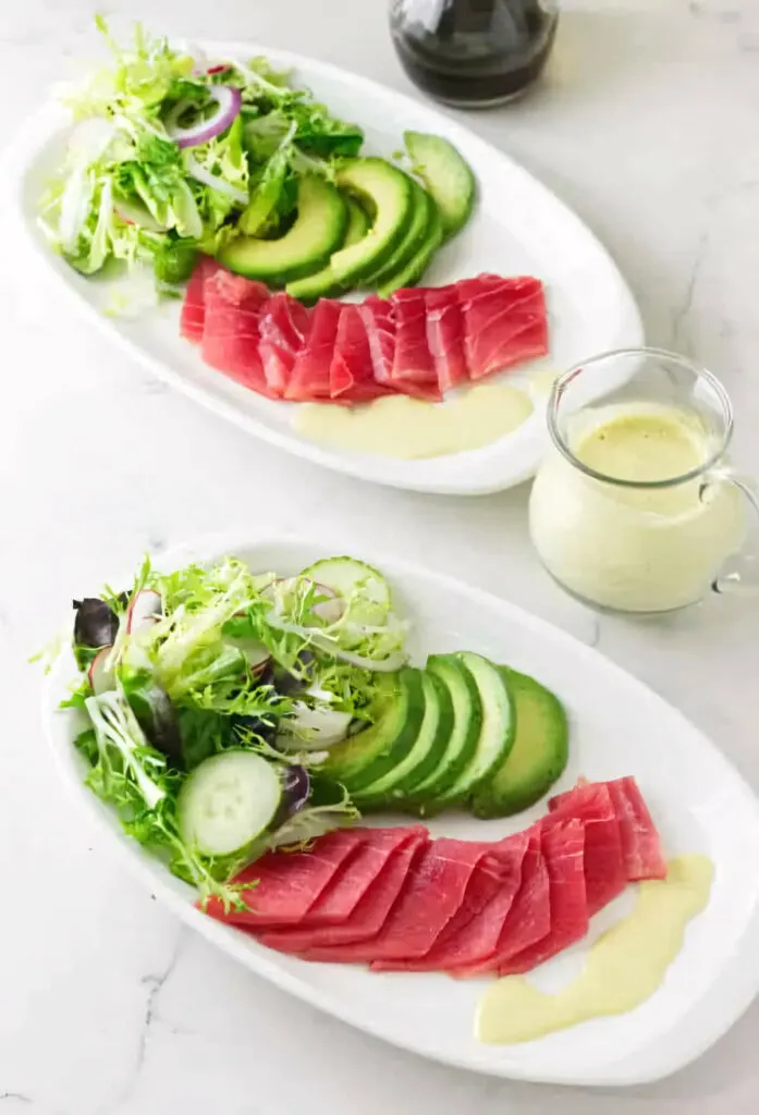 Two plates filled with a sashimi salad next to a pitcher of wasabi emulsion.