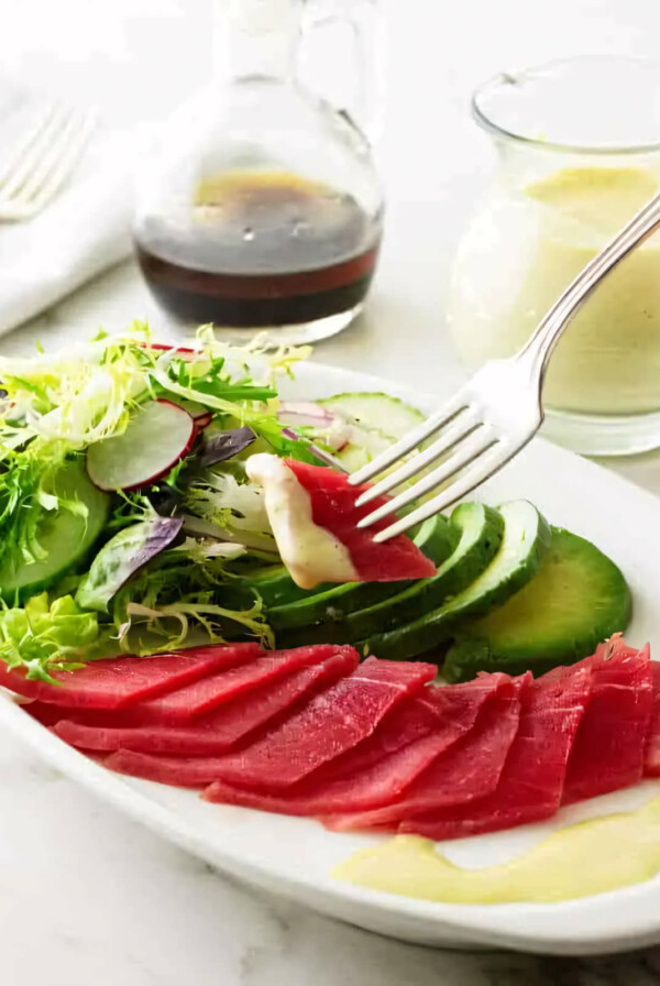 A fork grabbing a bite of tuna sashimi and dipping it in wasabi dressing.