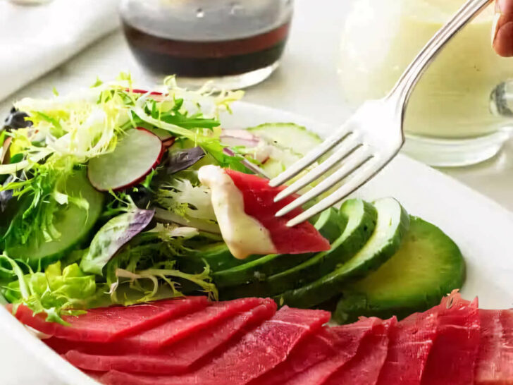 A fork grabbing a bite of tuna sashimi and dipping it in wasabi dressing.