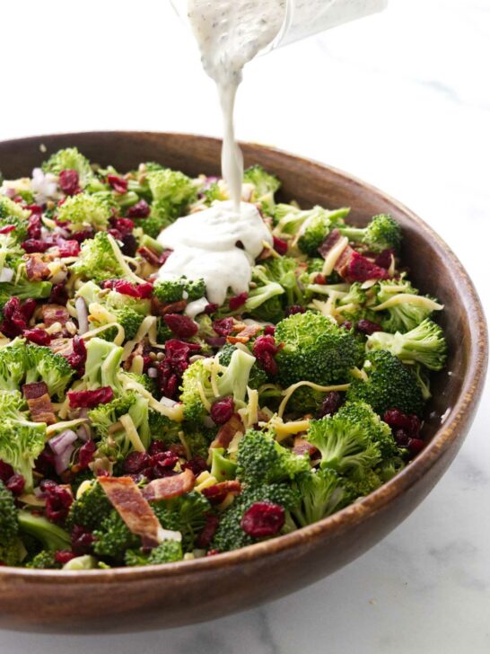 Pouring dressing over the broccoli salad with cranberries.