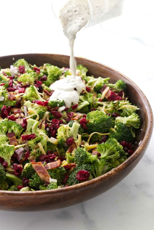 Pouring dressing over the broccoli salad with cranberries.