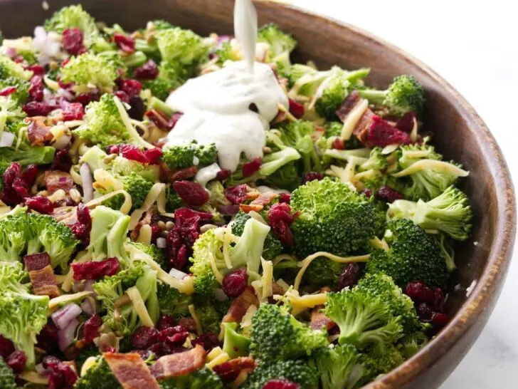 Pouring dressing over the broccoli salad with cranberries.