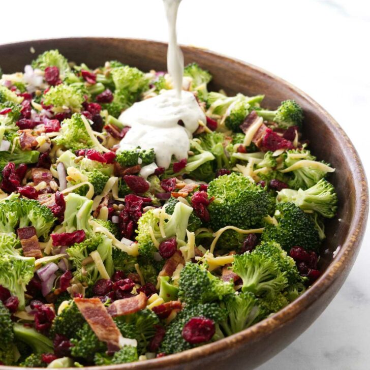 Pouring dressing over the broccoli salad with cranberries.