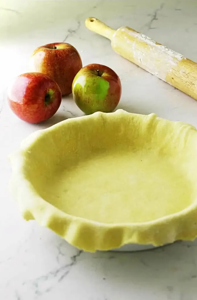 Einkorn pie dough in a pie plate next to a rolling pin.