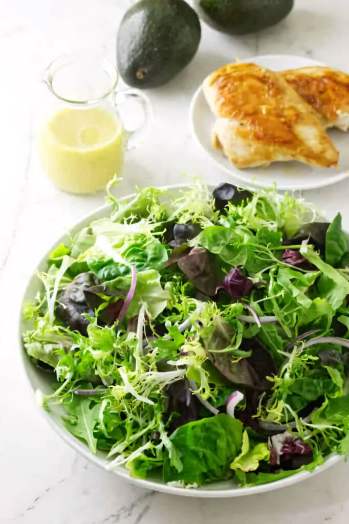 Mixed greens with chicken and avocado in the background.