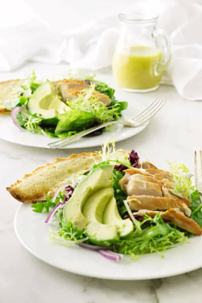 A crisp green salad with avocado and chicken on a plate with bread.