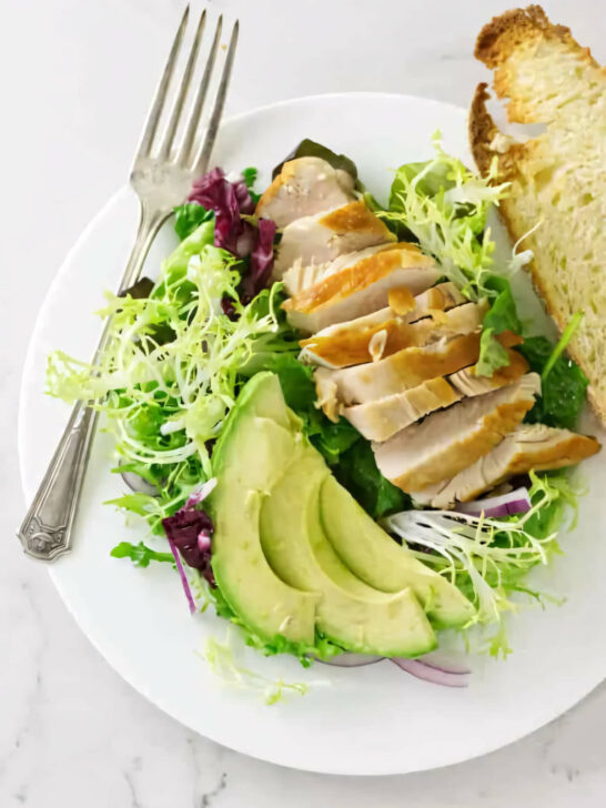 A plate filled with chicken and avocado salad with mixed greens.