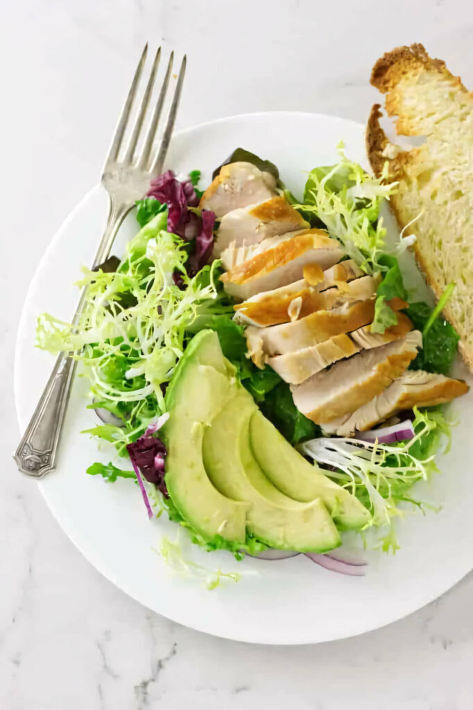 A plate filled with chicken and avocado salad with mixed greens.