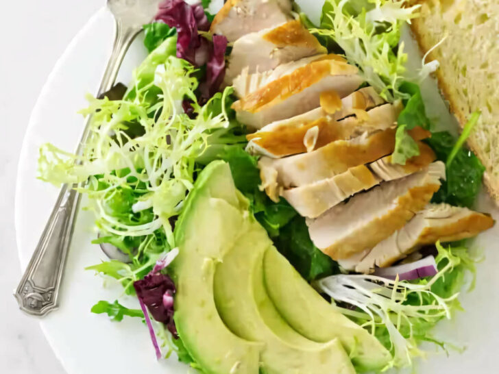 A plate filled with chicken and avocado salad with mixed greens.