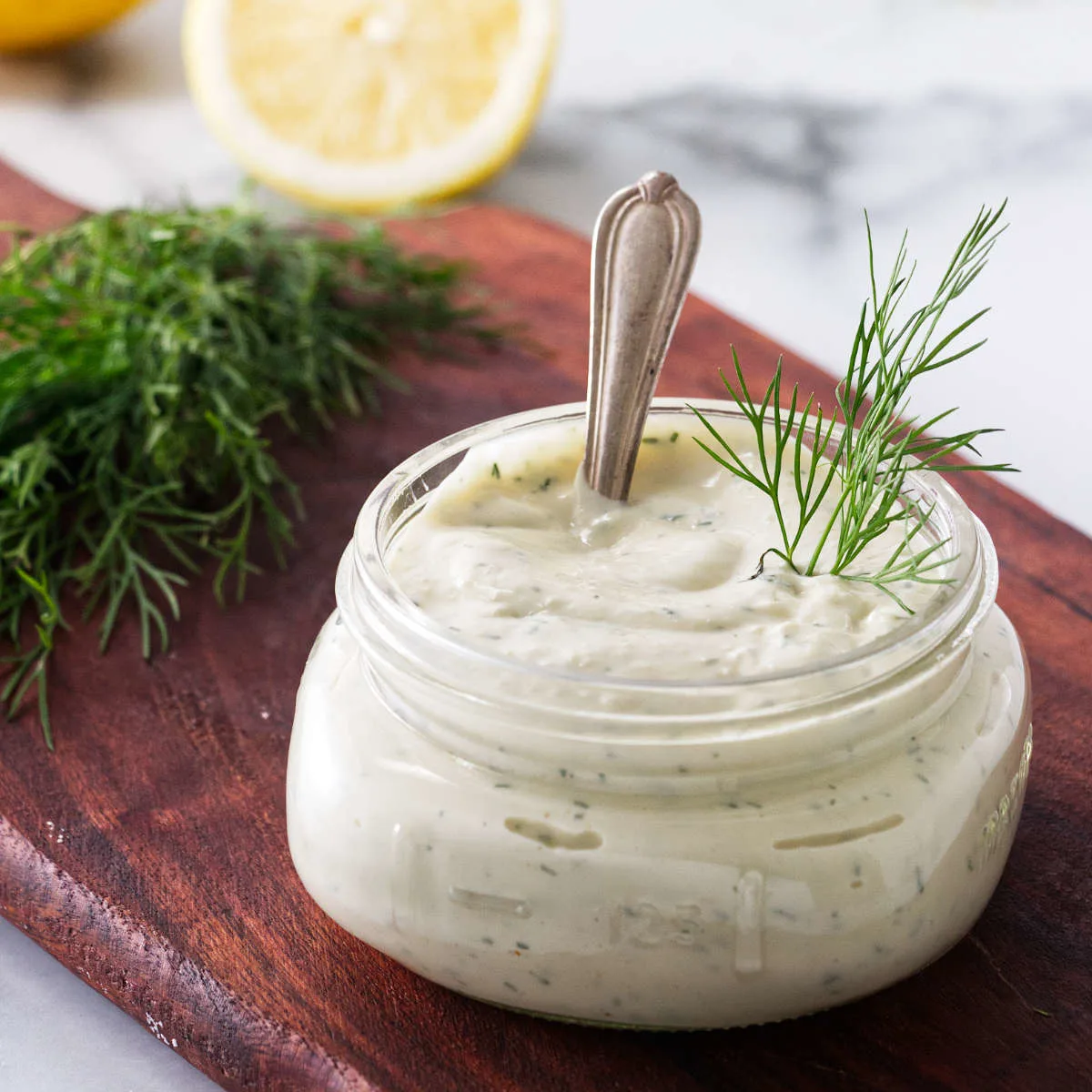 Homemade dill mayo on a kitchen counter next to a sprig of dill.