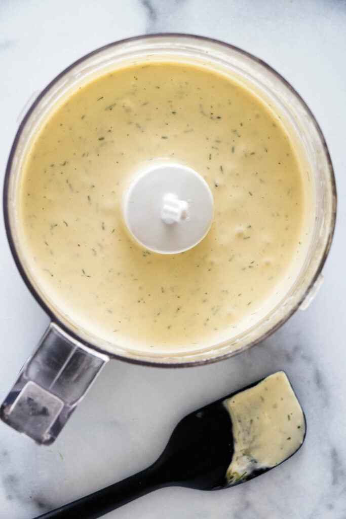 A food processor with lemon and garlic dill aioli next to a spatula.