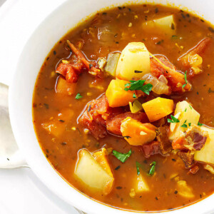 A bowl of red clam chowder with veggies.