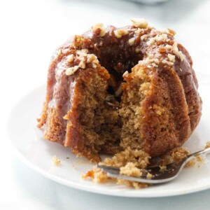 A mini apple bundt cake with caramel sauce on top and next to a fork.