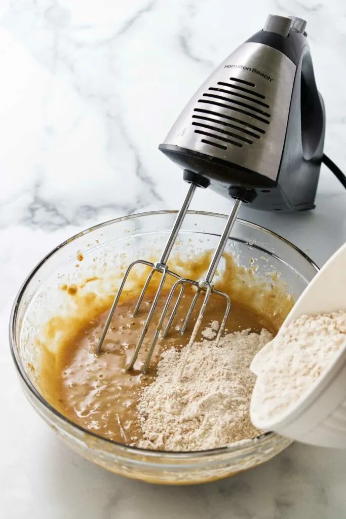 Slowly adding flour to apple cake batter.