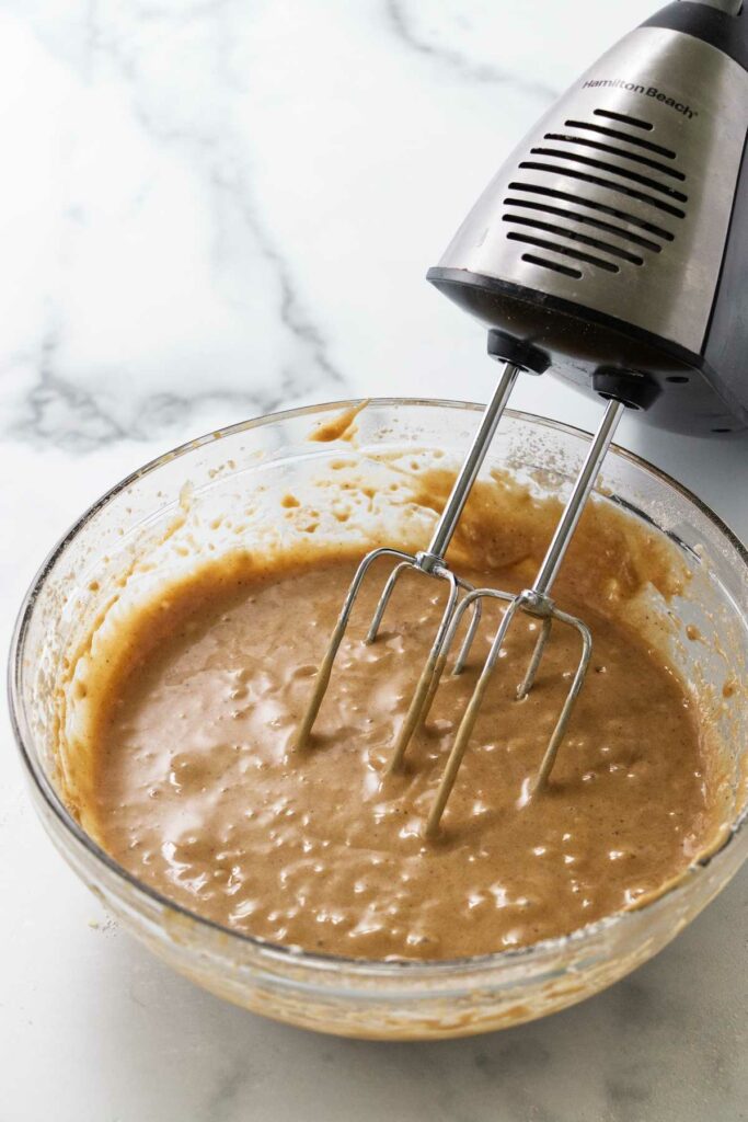 A mixer next to a bowl of apple cake batter.