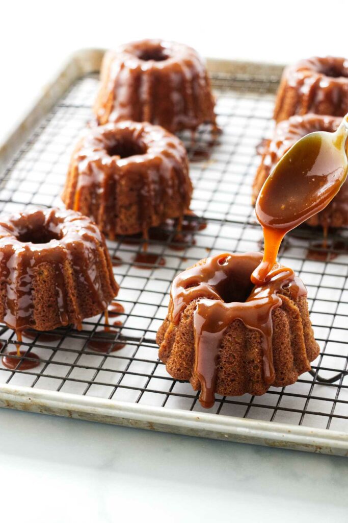 Drizzling caramel sauce on several mini apple bund cakes.