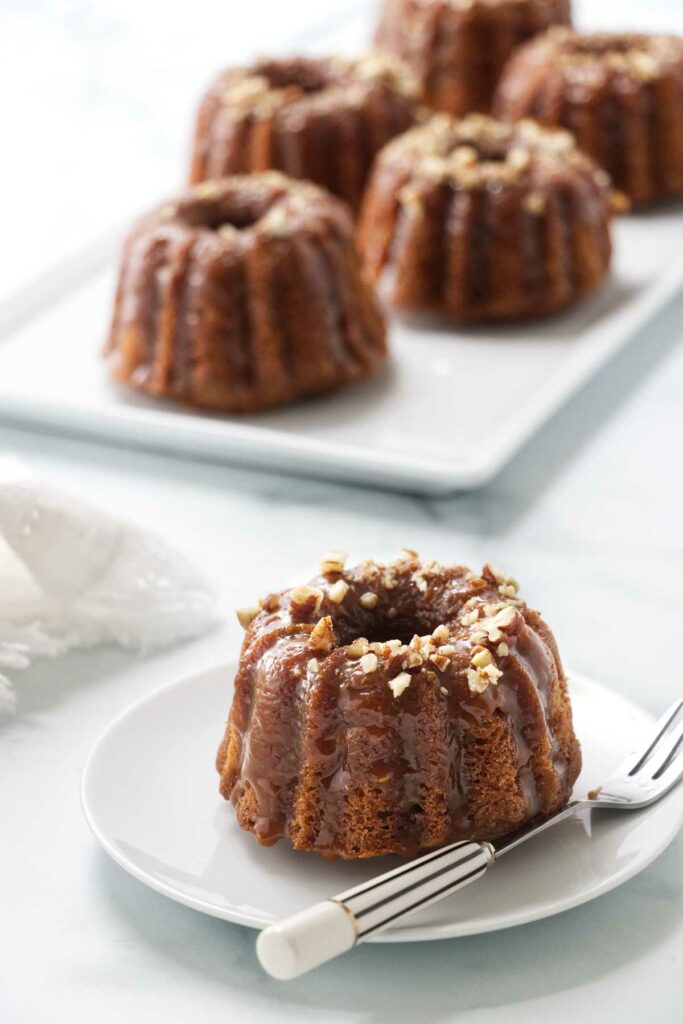 A small apple cake on a plate in front of a platter of mini cakes.