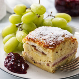 A slice of a monte cristo breakfast casserole on a plate with grapes.