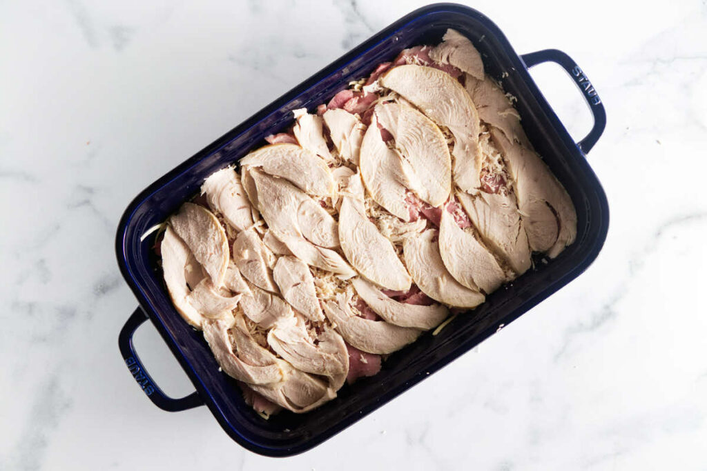 Layering slices of turkey in a baking dish.