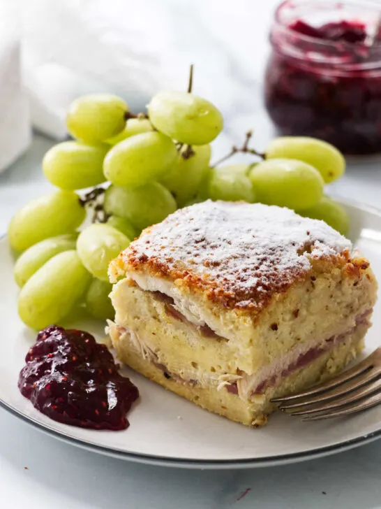 A slice of monte cristo casserole on a plate with green grapes.