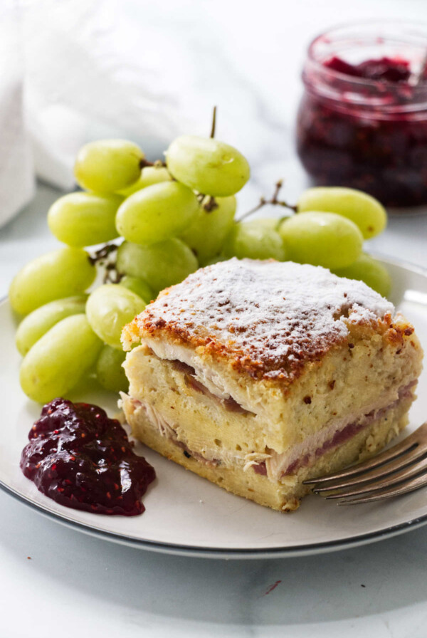 A slice of monte cristo casserole on a plate with green grapes.