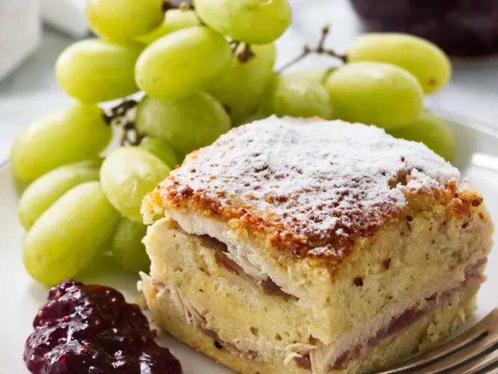 A slice of monte cristo casserole on a plate with green grapes.