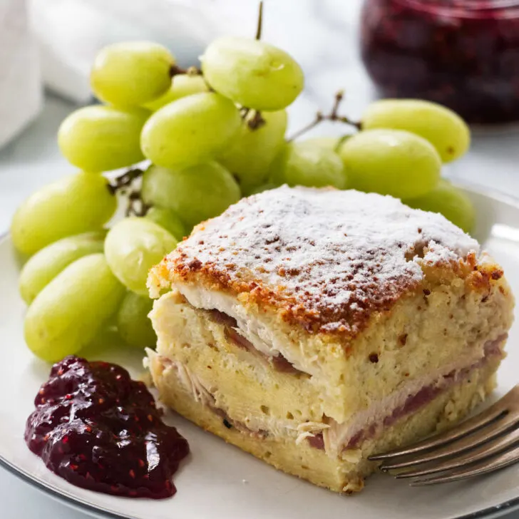 A slice of monte cristo casserole on a plate with green grapes.