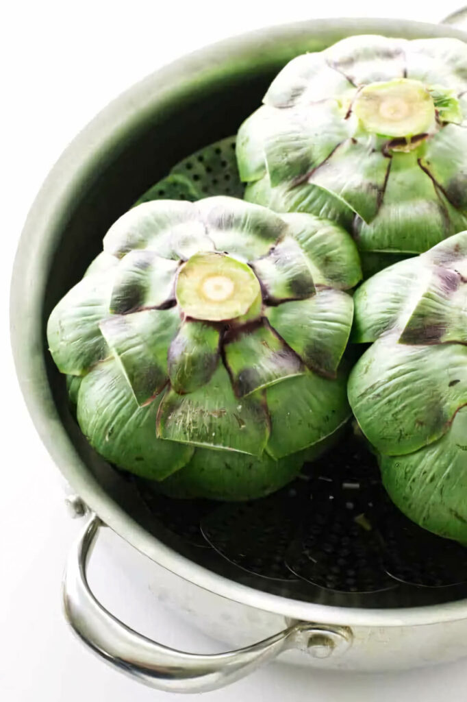 Fresh artichokes in a steamer basket on the stove.