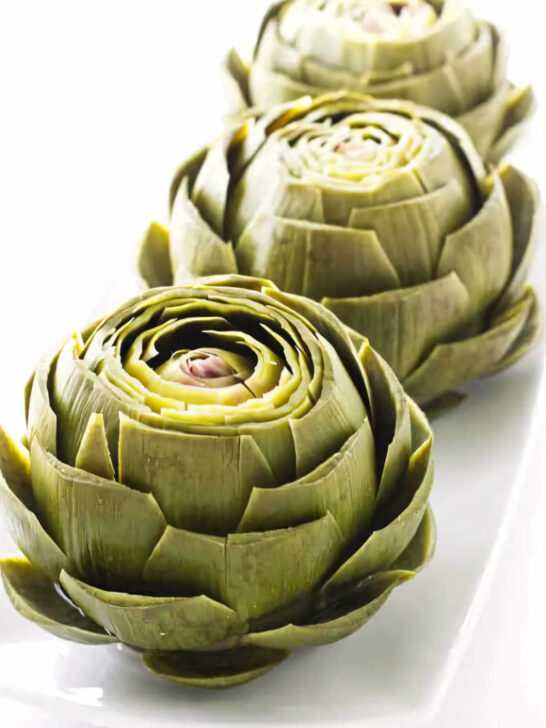 Several steamed artichokes on a serving platter.