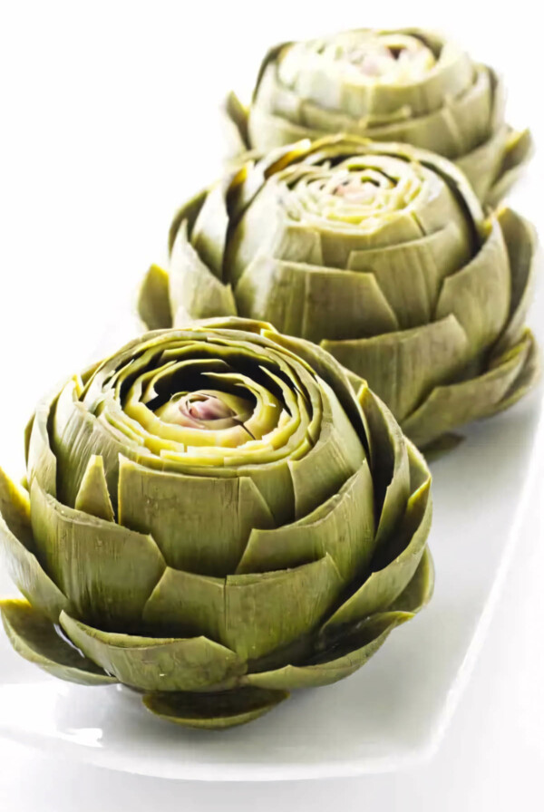 Several steamed artichokes on a serving platter.