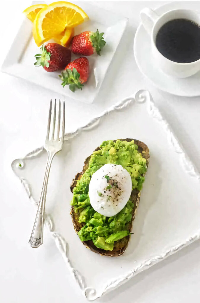 A poached egg on avocado toast next to coffee and fruit.