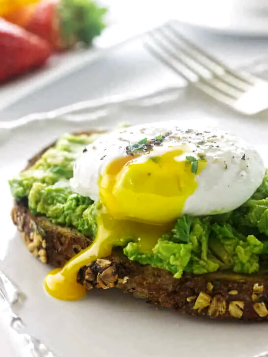 Avocado toast with a poached egg on a plate with a fork.