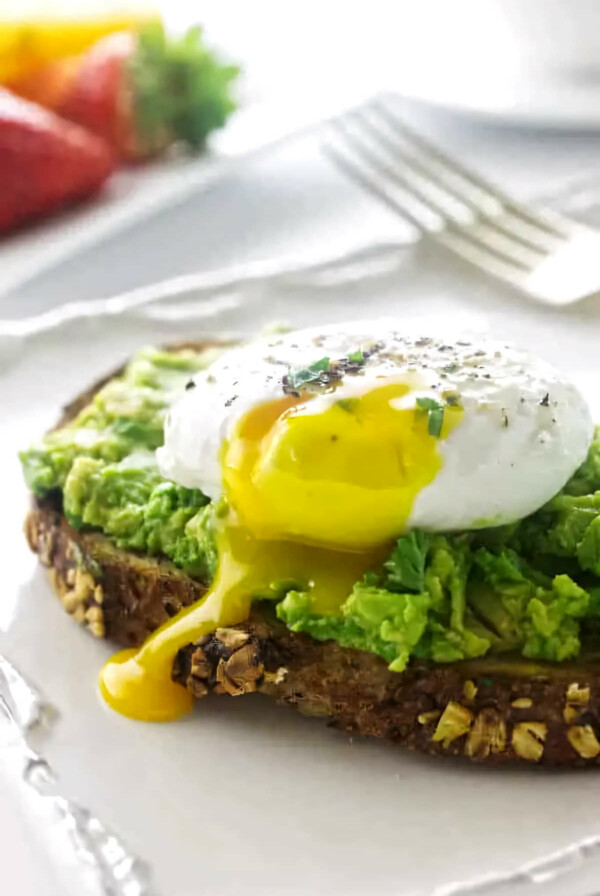 Avocado toast with a poached egg on a plate with a fork.