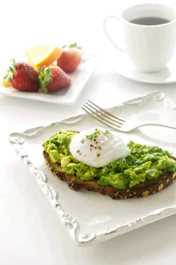 Avocado toast with a poached egg next to a plate of fruit.