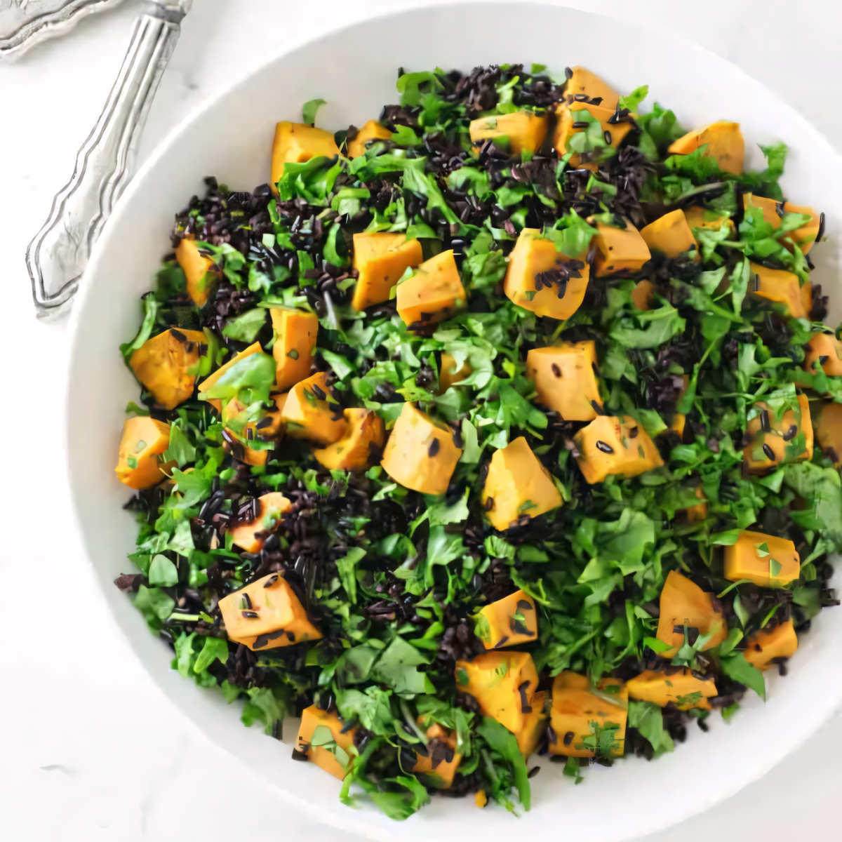 A serving bowl with black rice and sweet potato salad and green kale.