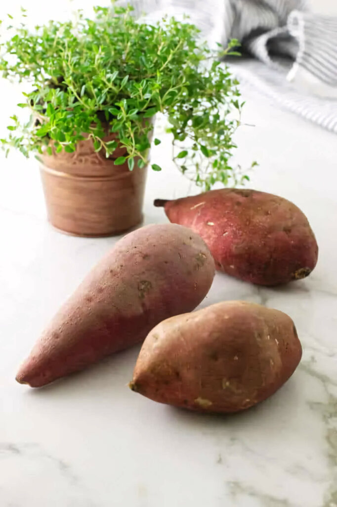 Several sweet potatoes next to a pot of fresh thyme.