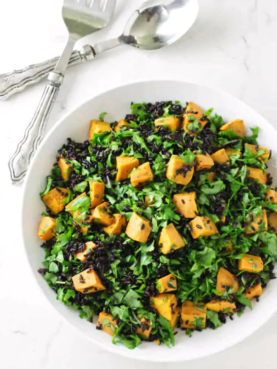 A salad bowl filled with chunks of sweet potato, black rice, and kale.