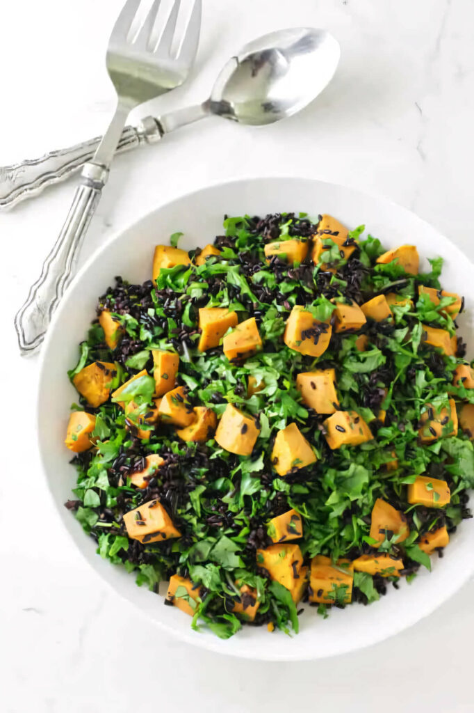 A salad bowl filled with chunks of sweet potato, black rice, and kale.