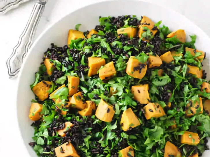 A salad bowl filled with chunks of sweet potato, black rice, and kale.