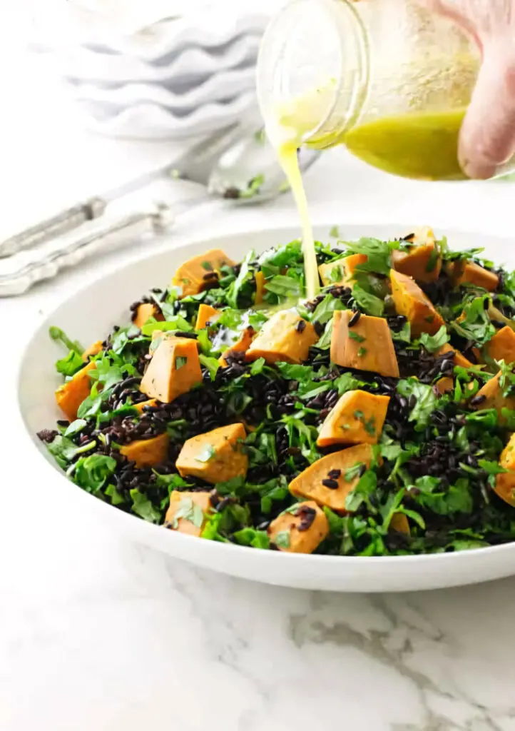 Pouring vinaigrette over a black rice sweet potato salad.