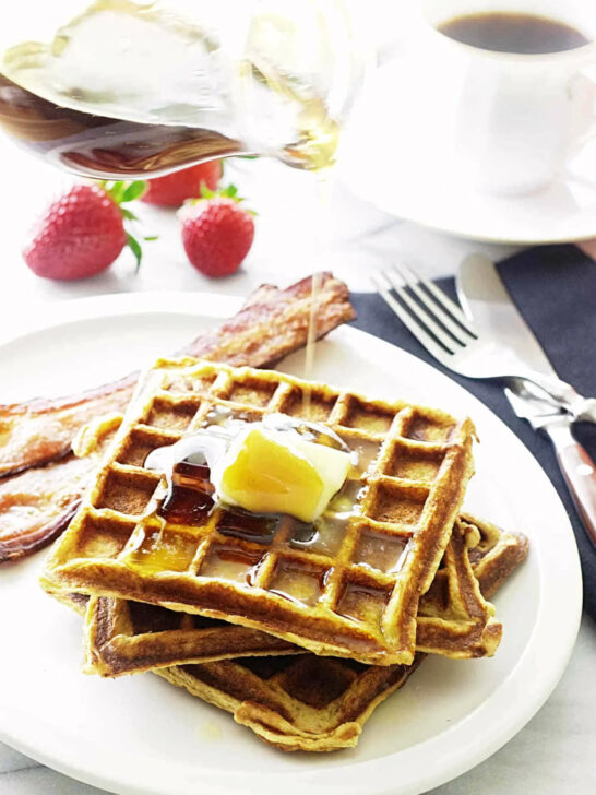 Three kamut waffles on a plate with bacon.