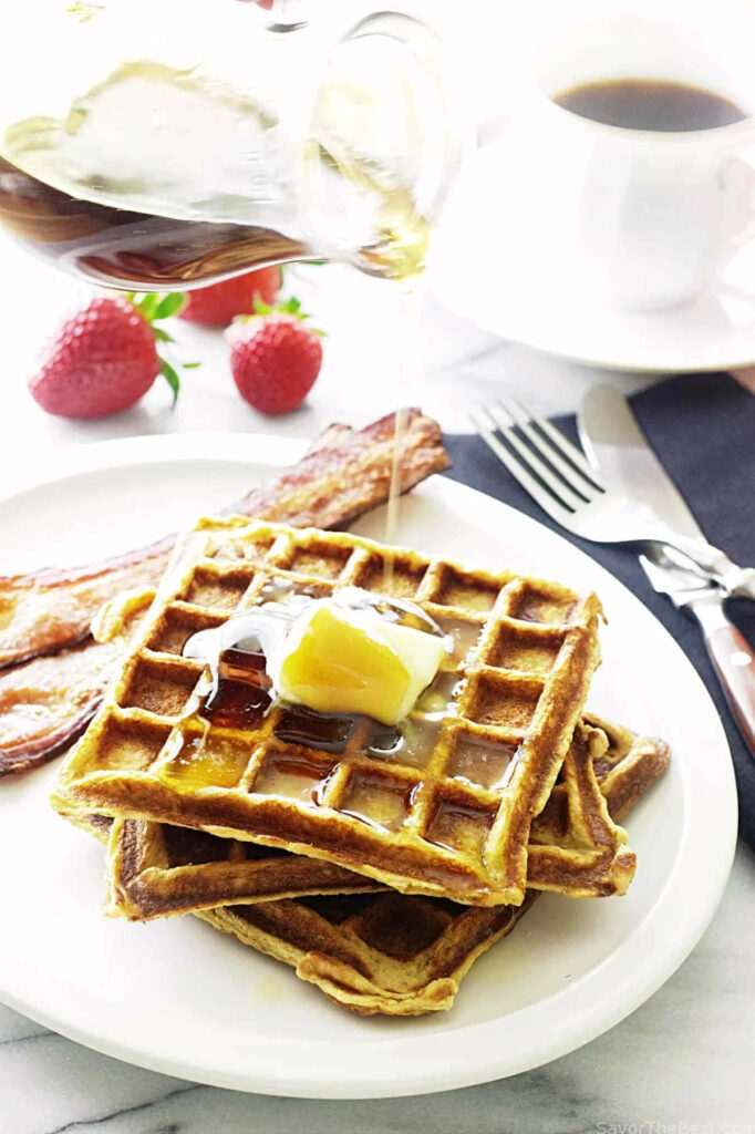 Three kamut waffles on a plate with bacon.