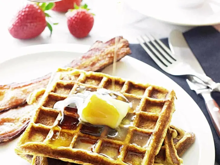 Three kamut waffles on a plate with bacon.