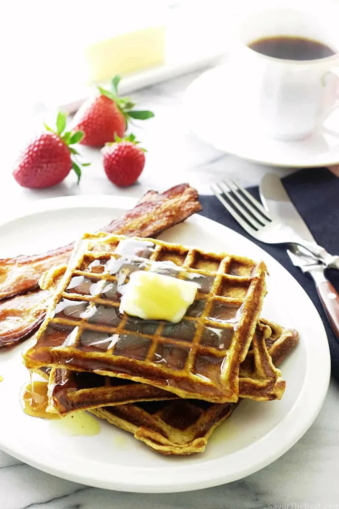 Several kamut flour waffles on a plate with strawberries and coffee in the background.