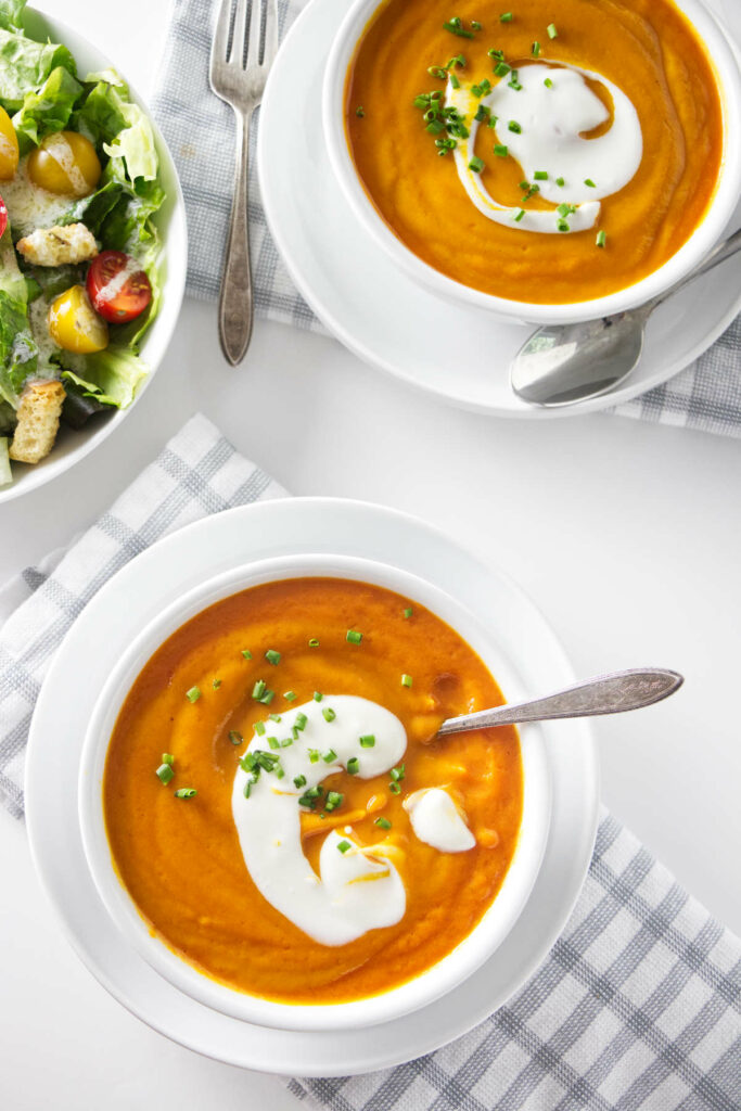 Two bowls of carrot soup next to a salad.