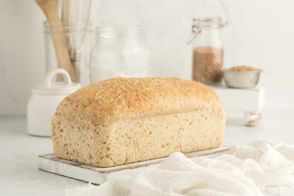 A freshly baked loaf of bread in front of a jar of cracked wheat.