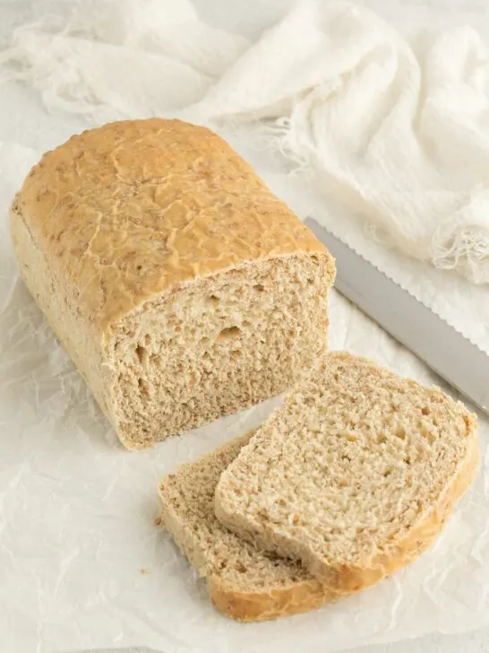 A partially sliced loaf of cracked wheat bread next to a knife.