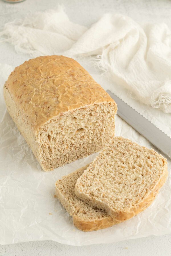 A partially sliced loaf of cracked wheat bread next to a knife.