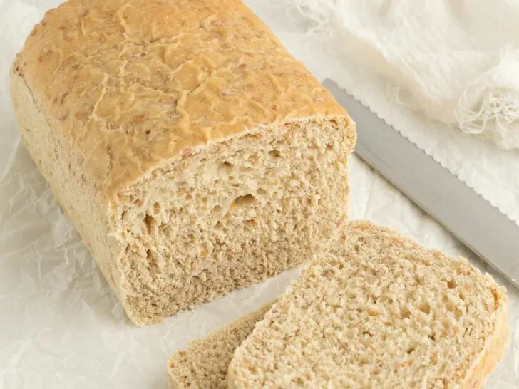 A partially sliced loaf of cracked wheat bread next to a knife.